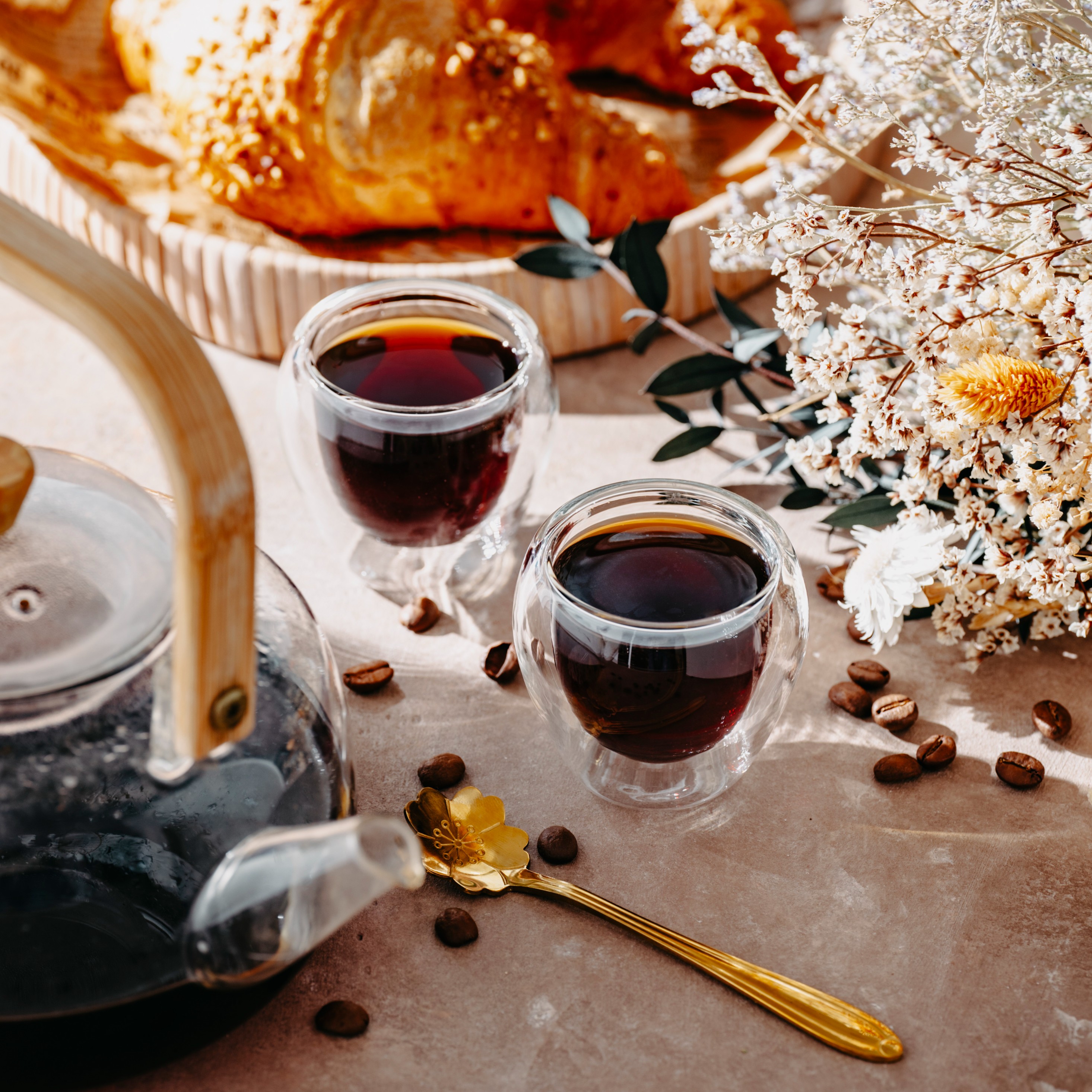 Dwie eleganckie, dwuścienne szklane filiżanki do espresso, napełnione ciemnym napojem, z ziarnami kawy w tle.