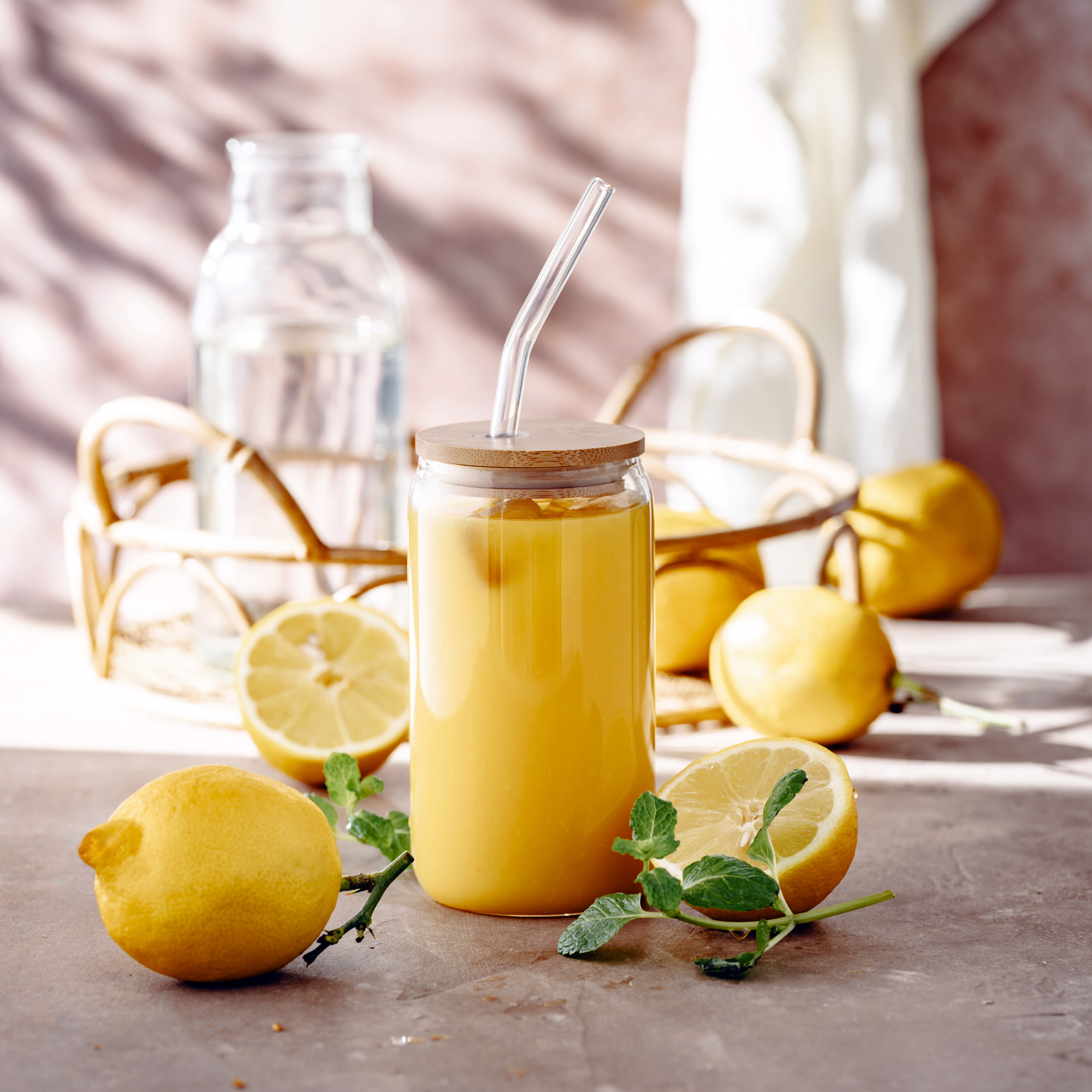 Szklany kubek z bambusową pokrywką i szklaną słomką, napełniony kawą mrożoną lub smoothie, na tle ziaren kawy.